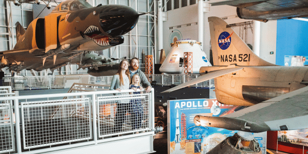 Family looks in awe of the real aircraft just feet away from them. Taken inside the center with space shuttles in the background.