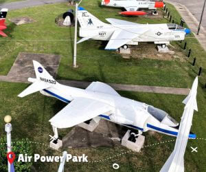 Fighter jets and airplanes on lawn near sidewalk.